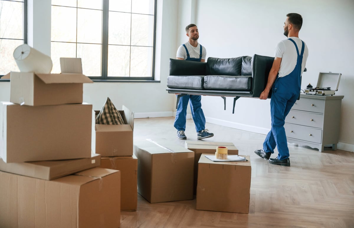 Two moving service employees carrying a heavy sofa inside a room